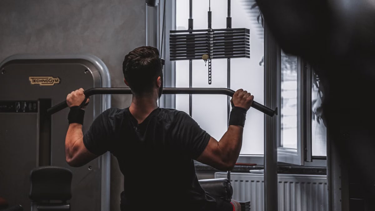 Back view of a man exercising with lat pulldown machine in the gym.